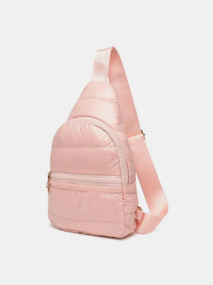 Glossy padded sling bag in pink with adjustable strap and zippered pockets.
