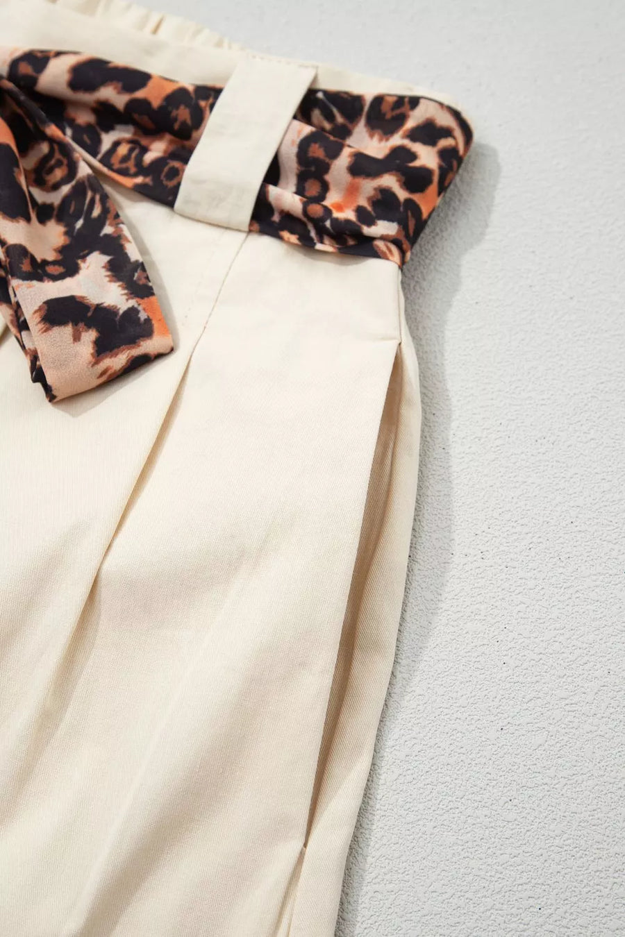 Cream wide-leg pants with leopard print sash belt and side pockets.