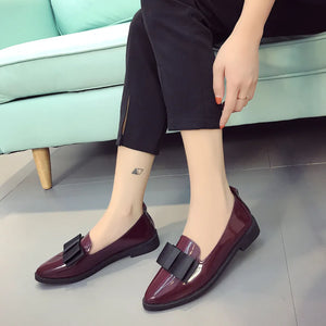 Patent leather loafers in burgundy with black bow detail.