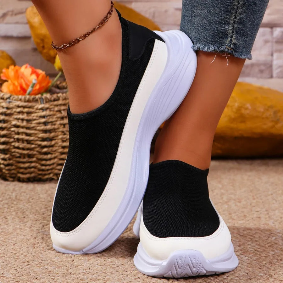 Black mesh slip-on sneakers with white accents and a white sole.