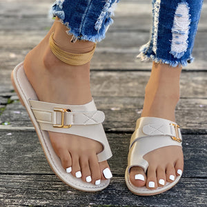 Beige toe loop flat sandals with gold buckle detail, casual style.
