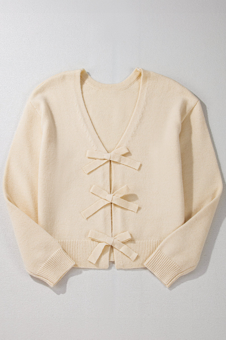 Ivory bouclé knit cardigan with v-neck and three front bow details.