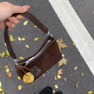 Brown suede crossbody bag with pompom charms and adjustable strap