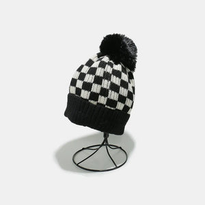 Checkerboard knit beanie with black faux fur pom and ribbed band.
