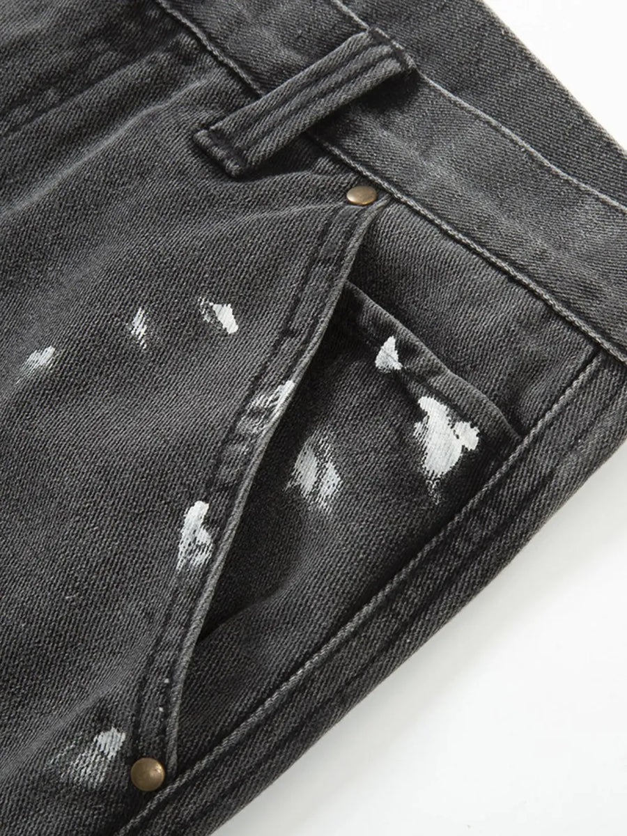Dark gray bootcut jeans with white paint splatters and brass button details.