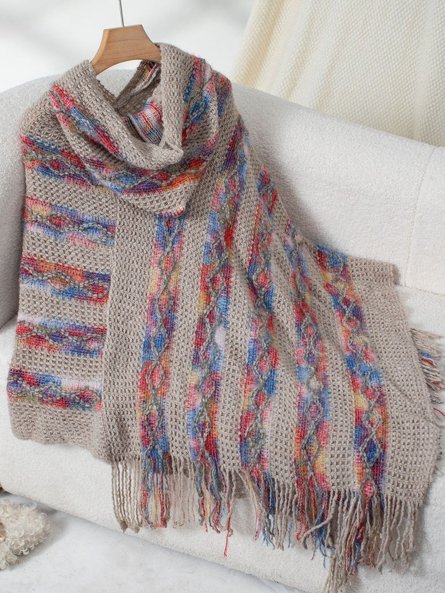 Textured knit hooded cape in beige with colorful striped and cable knit details and fringe.