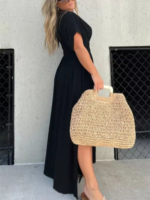 Black V-neck maxi dress with dolman sleeves and smocked waist, worn with a straw bag.