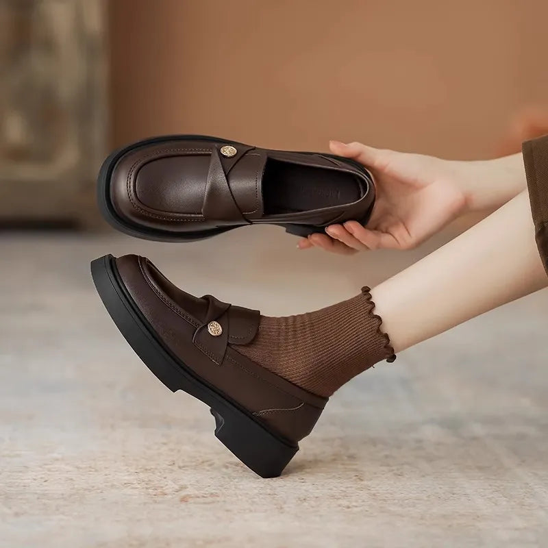 Coffee brown penny loafers with gold detail and crisscross strap, shown on foot and held.