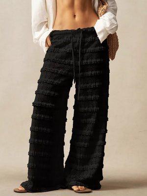 Black wide-leg pants with tiered ruffle detailing and a drawstring waist.