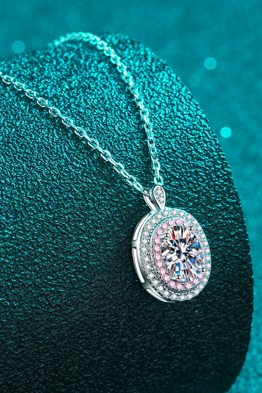 Silver halo moissanite pendant necklace with a round brilliant cut center stone and pink accent stones.