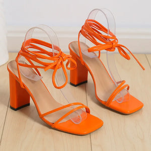 Orange lace-up square toe block heels with thin straps and clear accents.