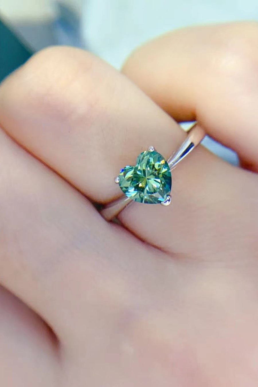 Green heart moissanite solitaire ring on a finger