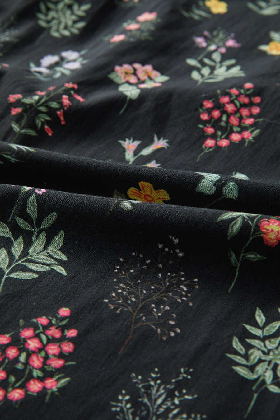 Black cotton blouse with a botanical floral print and short sleeves.