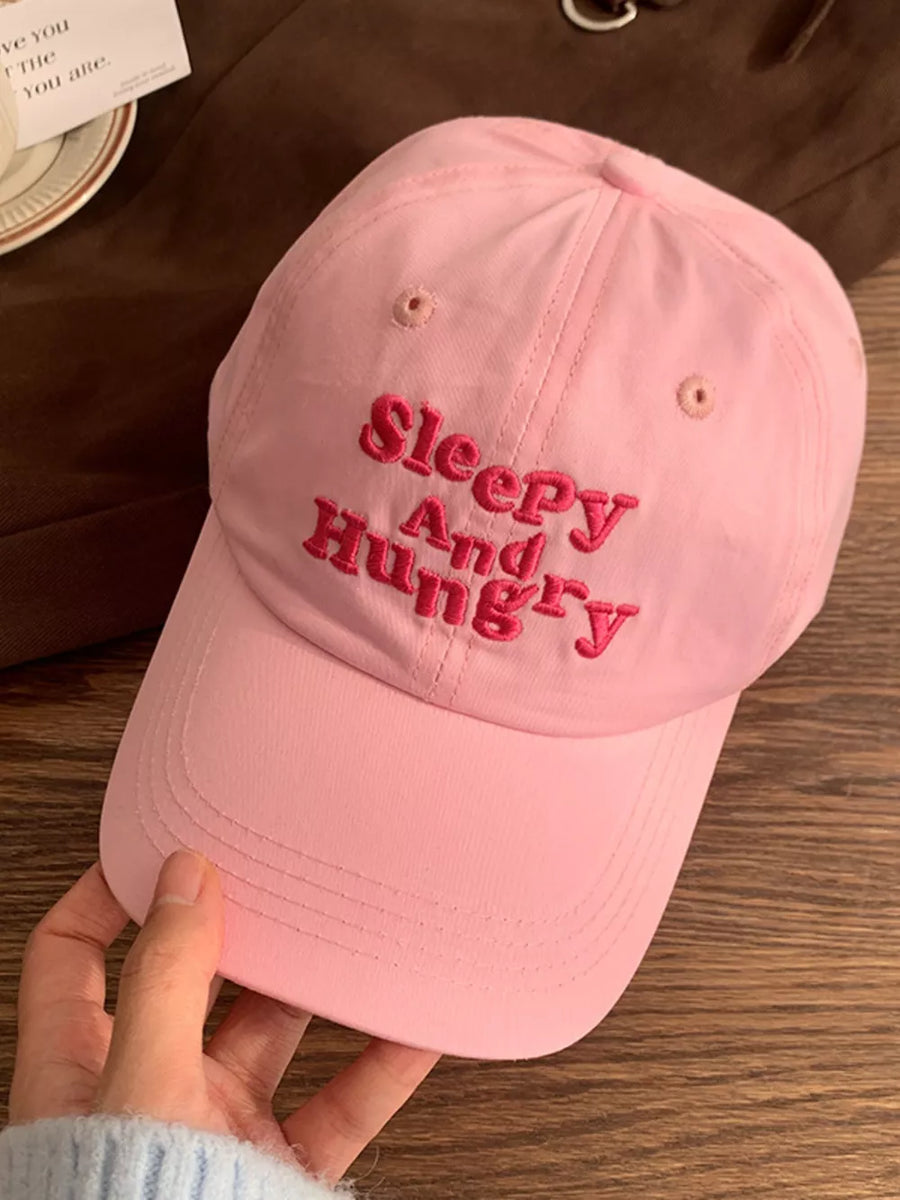 Pink cotton baseball cap with embroidered "Sleepy And Hungry" text.