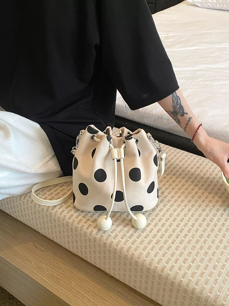 black crossbody bag featuring drawstring closure and polka dot