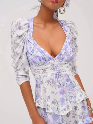 Ruched floral tie-front dress with puff sleeves and ruffled hem in purple and white.