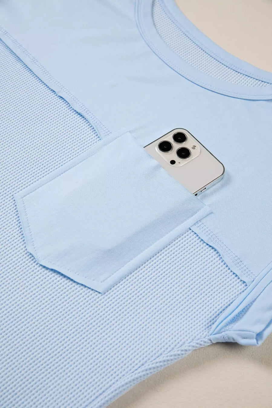 Light blue waffle knit t-shirt with pocket holding a phone and curved hem detail.