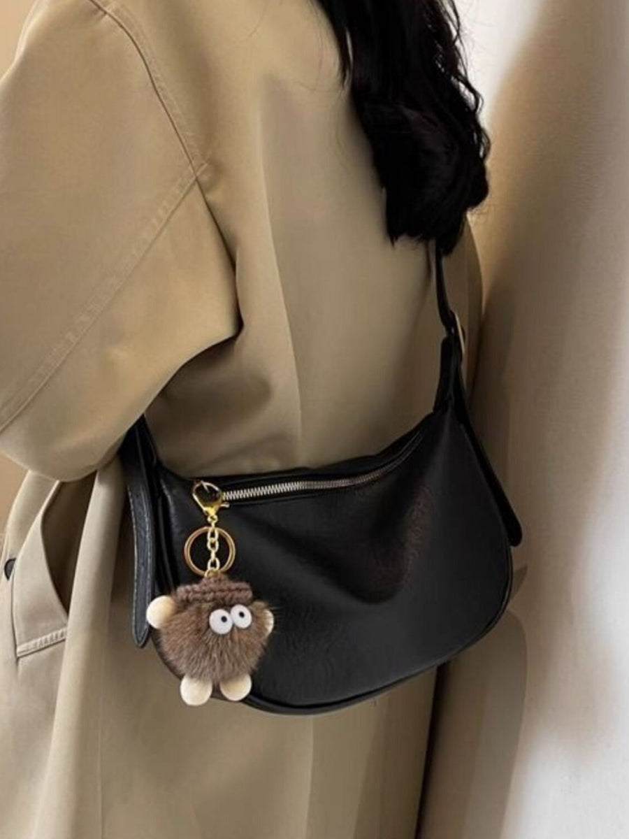 Black crescent shoulder bag with plush charm and adjustable strap