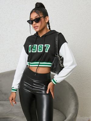 Black cropped hoodie with white sleeves, '87 graphic, and green striped trim.