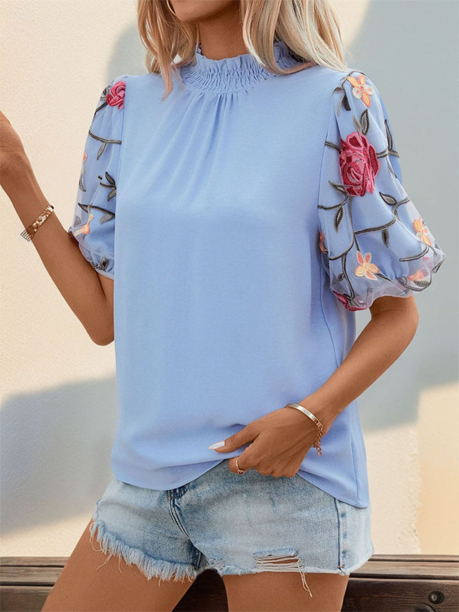 Light blue blouse with smocked mock neck and sheer organza sleeves with floral embroidery.