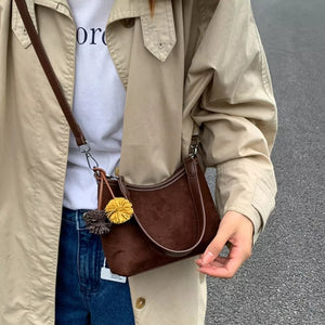 Brown suede crossbody bag with yellow pom-pom charm and adjustable strap.