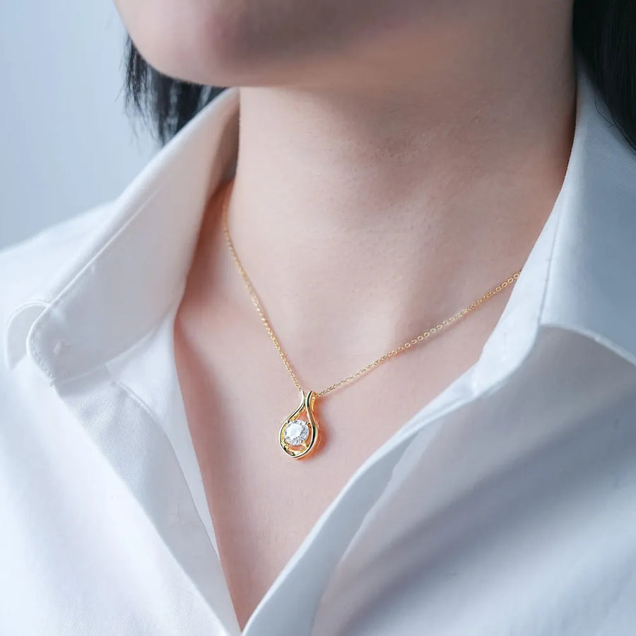Gold teardrop pendant necklace with moissanite stone on a woman wearing a white shirt.