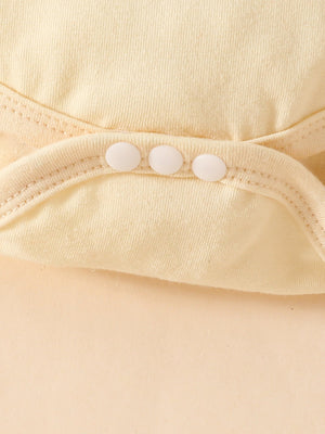 Baby bodysuit detail with three white snaps and ruffled trim in pale yellow cotton.
