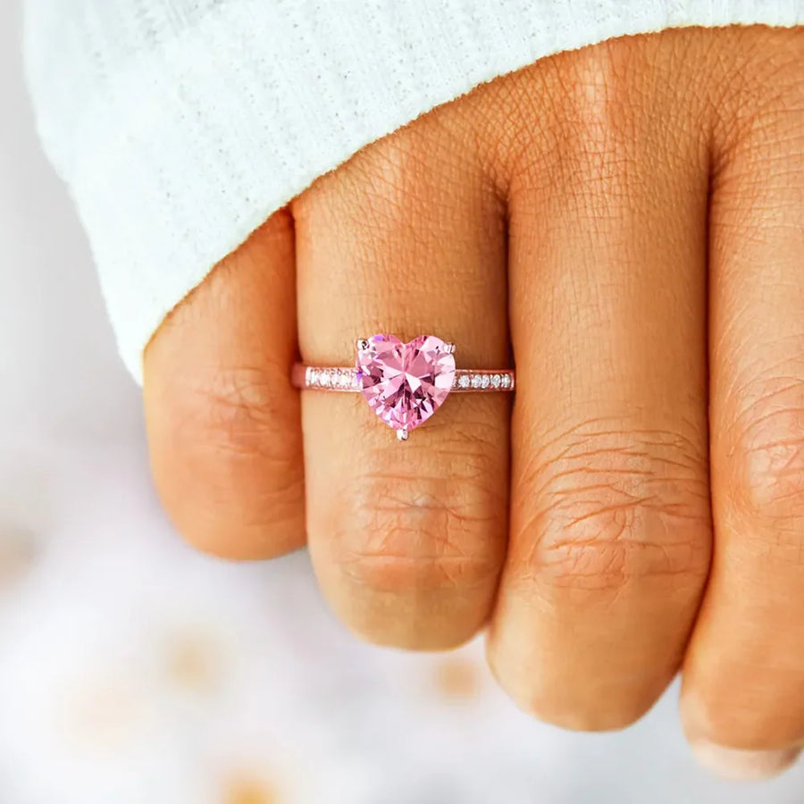 Rose gold ring with a pink heart cut pavé stone and small clear stones on the band.