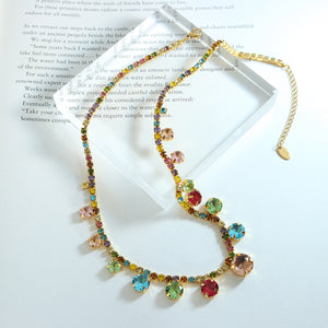 Gold chain necklace with a cascade of colorful faceted gemstones in round and heart shapes.