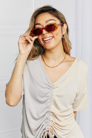 Tortoiseshell oval sunglasses with dark lenses, worn by a woman with a ruched two-tone top.