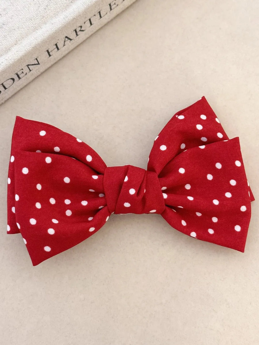 Deep red polka dot bow hair clip with a knotted center detail.