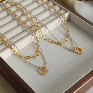 Gold layered chain necklace with beaded strand and twisted circle pendant.