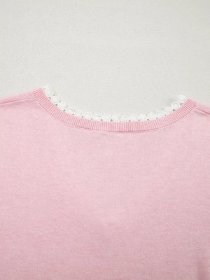 Pink knit top with delicate white lace trim at the V-neckline.