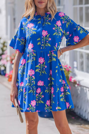 Tiered floral dress with pink flowers on blue cotton fabric, featuring ruffle sleeves and a tie neckline.