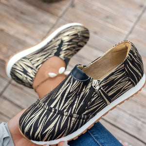 Zebra print slip-on flats with a side zipper detail in black and gold.