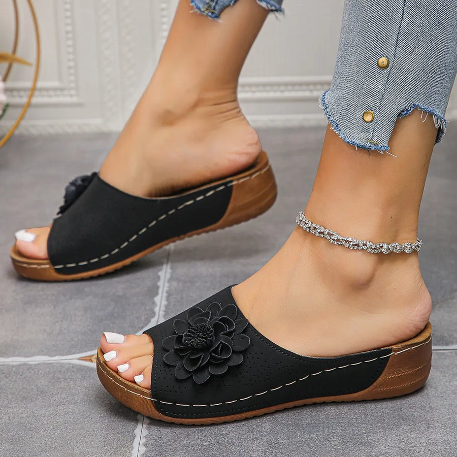 Black perforated floral wedge slides with contrast stitching and wooden sole.