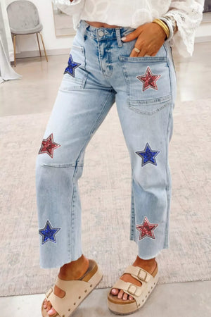 Light wash denim cropped utility jeans with red and blue sequin star patches and frayed hem.