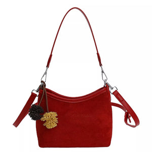 Red suede crossbody bag with two fluffy pom-pom charms and adjustable strap.