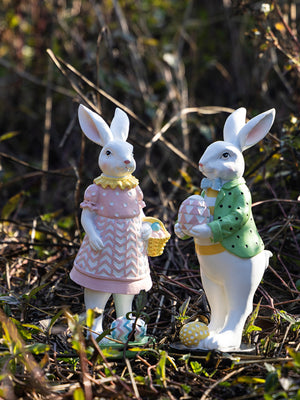 Easter bunny figurines in blush pink and gum leaf green holding eggs and baskets.