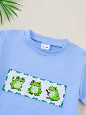 Light blue cotton baby t-shirt with three embroidered frogs on a white patch with green trim.
