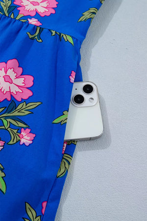 Tiered floral dress in blue with pink flowers, featuring a pocket holding a smartphone.