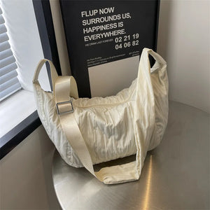 Quilted crescent shoulder bag in beige with adjustable strap and silver buckle detail.