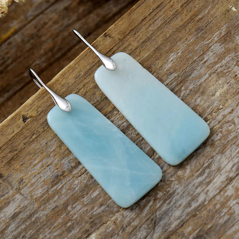 Aqua slab drop earrings with silver hooks on a wooden background.