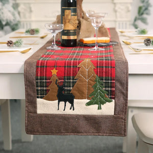 Festive plaid table runner in deep red with appliqué trees, deer, and star detail.