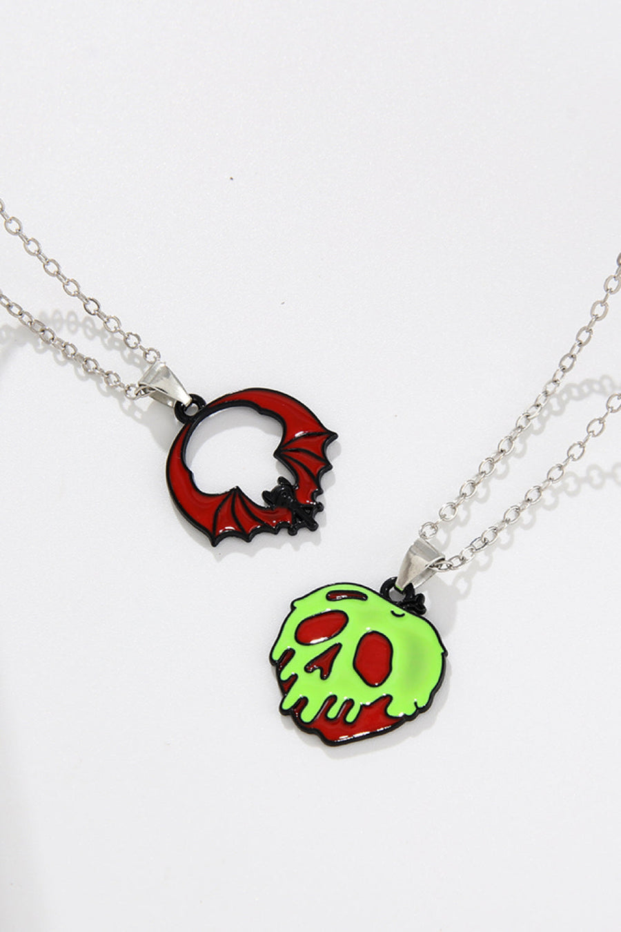Spooky Season enamel pendant necklaces, one red bat, one green skull with red accents.