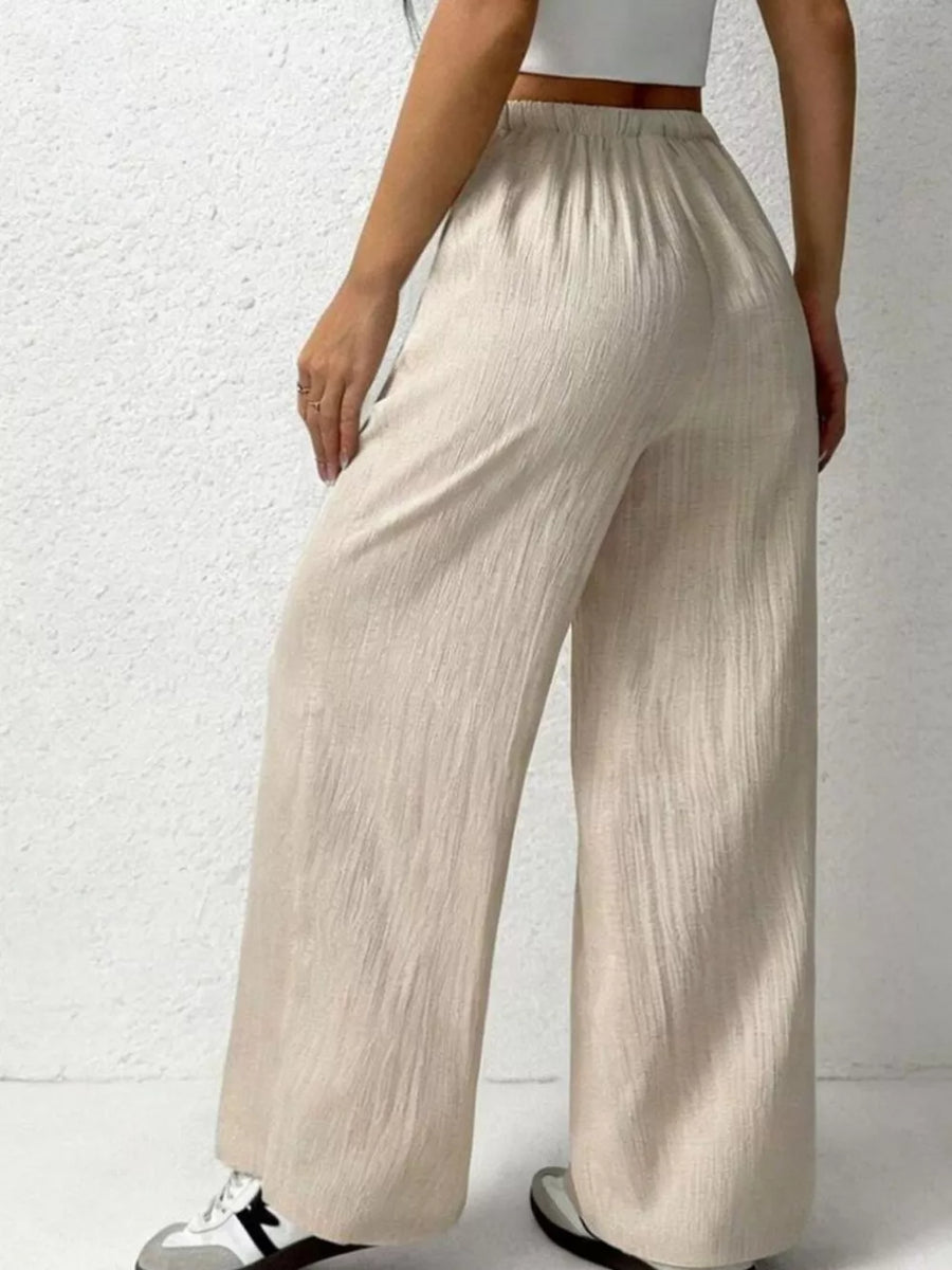 Relaxed beige cotton wide-leg pants with adjustable drawstring waist and textured fabric.