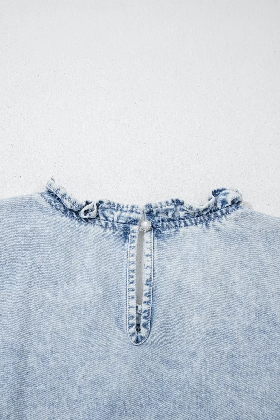 Light wash denim top with ruffled neckline and pearl button back closure