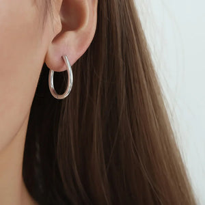 Silver oval hoop earrings with a subtle pearl drop detail.