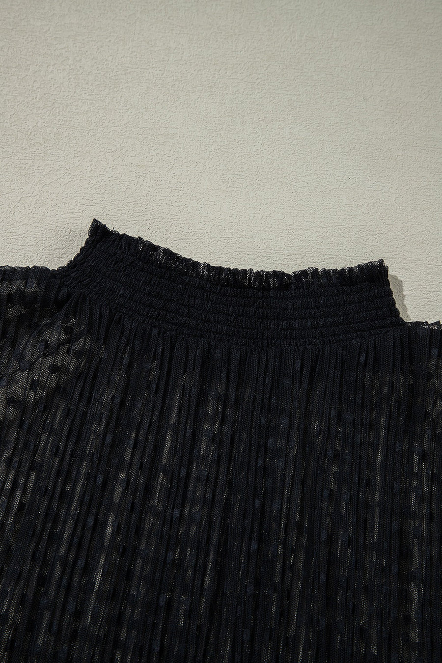 Black sheer mock neck blouse with textured dots and smocked neckline.