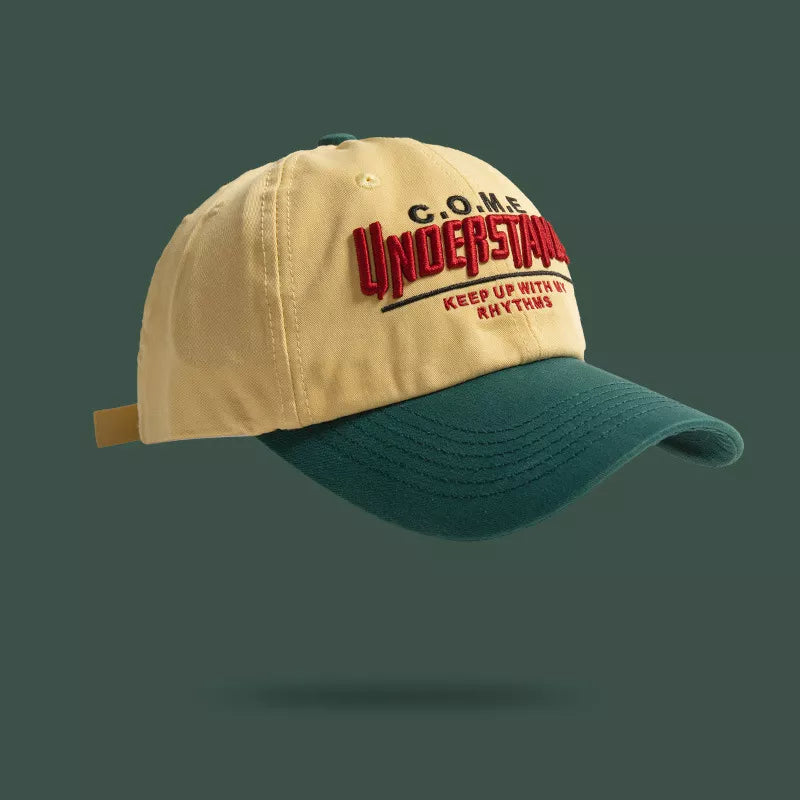 Embroidered baseball cap in tan with green brim and red text detail.